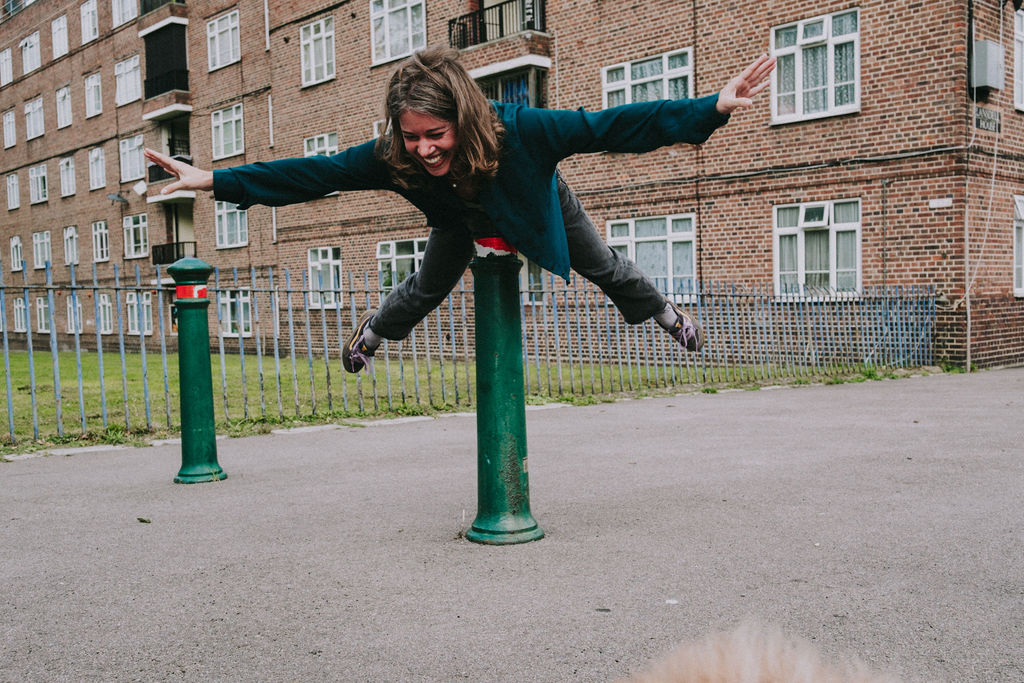 girl smiling while balancing her body horizontally using a traffic pole as support